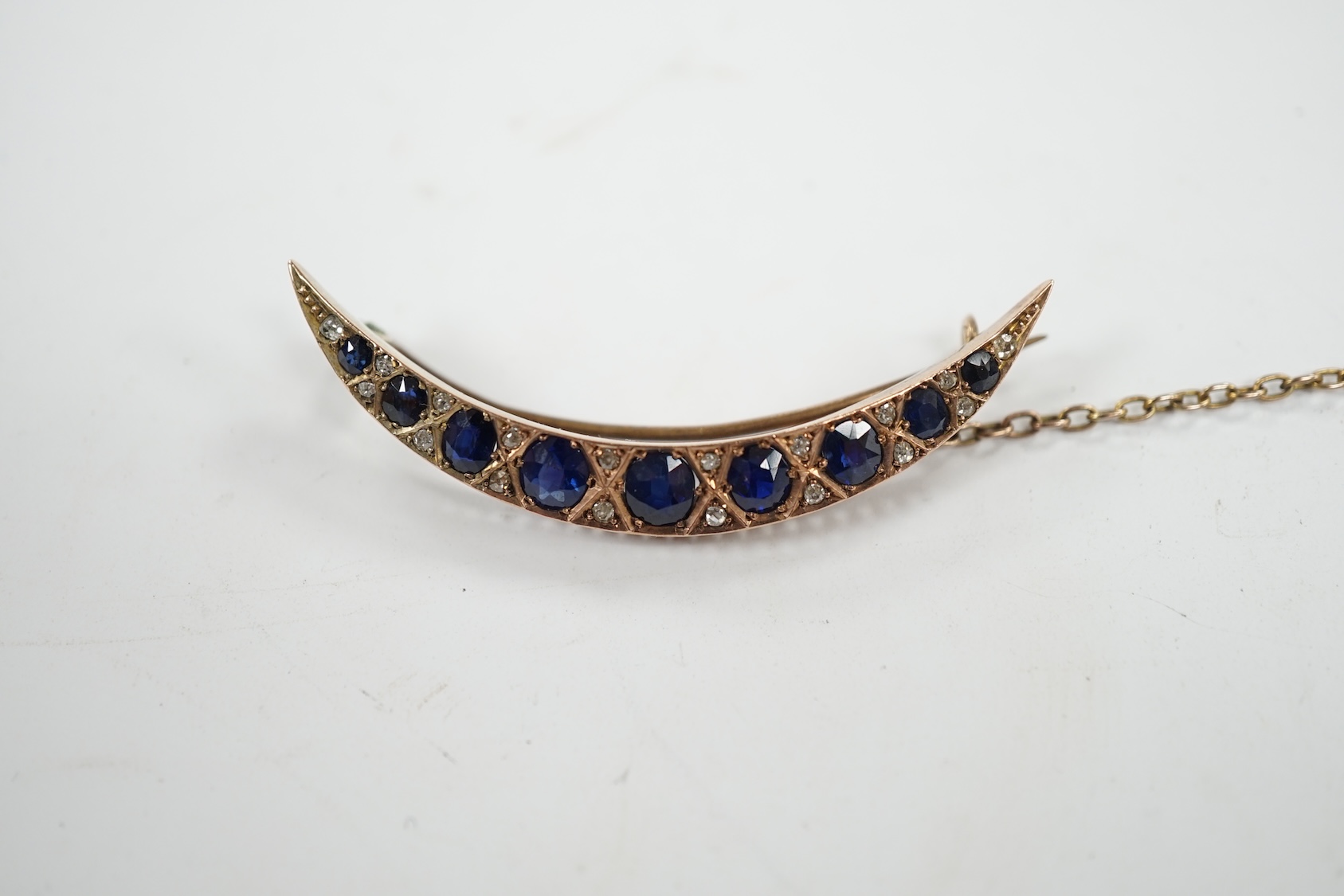 An early 20th century yellow metal, graduated sapphire set crescent brooch, with diamond chip spacers, 49mm, gross weight 5.8 grams. Condition - fair to good